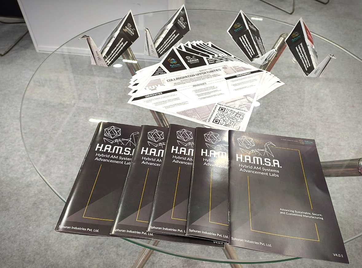 HAMSA origami brochures folded into swans on a glass table at the AM Conclave booth, with the marketing booklets in the foreground